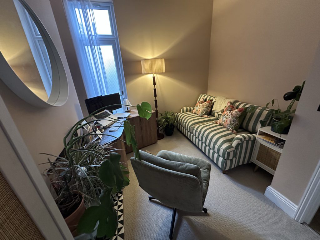 A wide view of the therapy room, with a sofa, armchair and soft lamp light