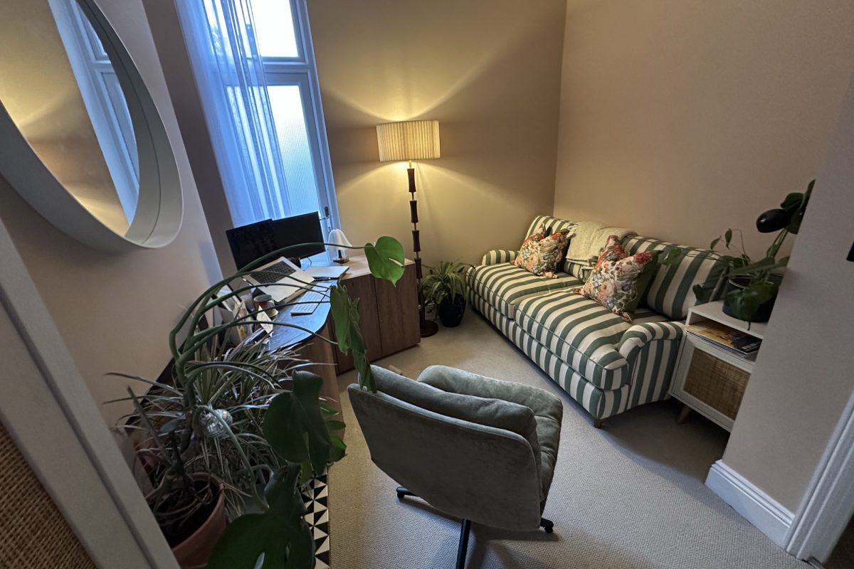 A wide view of the therapy room, with a sofa, armchair and soft lamp light